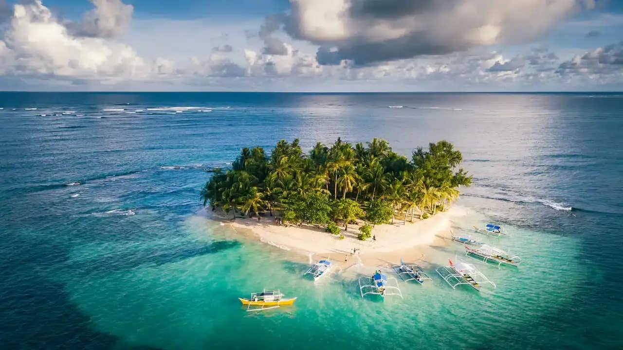 Eine kleine tropische Insel mit üppigen Palmen, türkisfarbenem Wasser und vor Anker liegenden Booten, perfekt für ein idyllisches Inselhopping-Abenteuer.