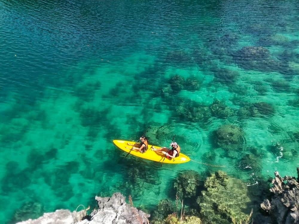 Two people paddle in a yellow kayak over the clear turquoise waters of El Nido, revealing rocks and coral beneath the surface. This vibrant Palawan scene conveys a sense of adventure and tranquility, perfect for island hopping enthusiasts seeking hidden wonders.