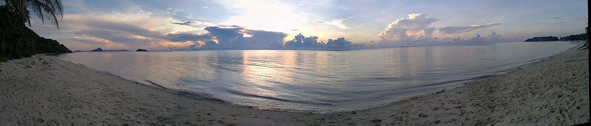 Panoramic view of a tranquil beach in Palawan at sunset, with calm waves, distant islands, and scattered clouds in the sky.