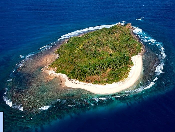 Aerial view of a small tropical island surrounded by vibrant blue ocean, perfect for a boat trip adventure, with lush greenery and a sandy shoreline.